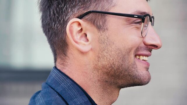side view of handsome man in glasses smiling while talking outside