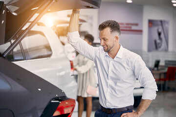 young caucasian customer man is opening car trunk in dealership, examine it before buying