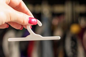 A miniature plastic hanger in the hand of a woman against the background of a wardrobe with clothes.