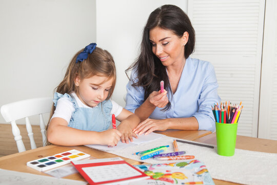 Smiling mother and daughter preparing for lessons and draws at the table with pencils and paints. Parent and pupil of preschool. First day of fall autumn. Girl from elementary class, back to school