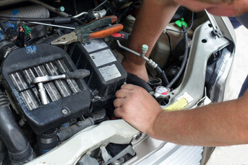 A man makes car repairs. Repairs something under the hood of a car.