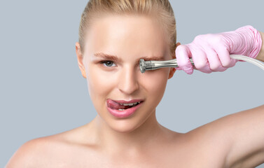Fototapeta premium Beautiful young blonde woman with nude makeup,clean fresh skin naked shoulders holds a nozzle for microdermabrasion in her hands.She will do cosmetic procedure microdermabrasion.Aesthetic cosmetology.
