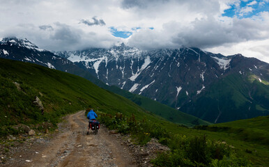 Fototapeta na wymiar Svanetia, Georgia: Cyclist rides a path with mountains in the background on a cloudy and stormy day