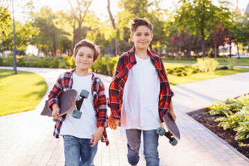 two pretty brothers of Caucasian nationality standing in the park with skateboards in hands....