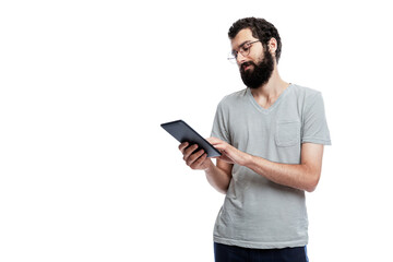 A young man in oracle and with a beard with a flat in his hands looks at the screen. Blogging, online communication and social networks. Space for text. Isolated on a white background.