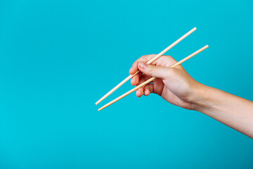 Hands holding chopsticks. Isolated on blue background, the place for caption and text