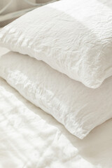 Closeup of white rough textile linen pillows. Beautiful bedding, morning light.