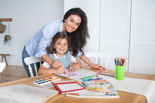 Smiling mother and daughter preparing for lessons and draws at the table with pencils and paints. Parent and pupil of preschool. First day of fall autumn. Girl from elementary class, back to school