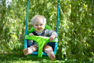 A little boy having fun playing on a swing under a tree in a garden