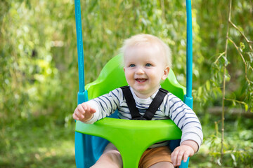 A little boy having fun playing on a swing under a tree in a garden