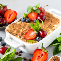 Classic Italian dessert Tiramisu decorated with strawberries, cherries and mint on a white background. Square