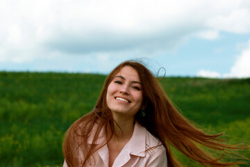 Naklejka premium Happy girl with flying hair on the field. Portrait of a smiling girl against a green field.