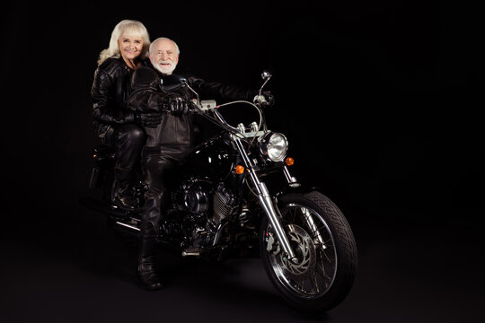 Portrait of his he her she nice attractive lovely cool free cheerful grey-haired rockers driving harley davidson chopper country world travelers isolated over black color background