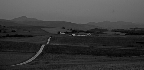 Defocused landscape of a meadow with a long road at night and mountains in the background