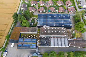 Aerial view of small factory with solar roofs surrounded by residential buildings