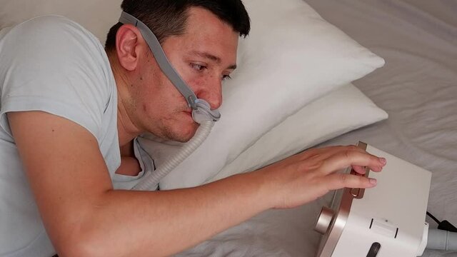 Close-up of healthy young adult man wearing under the nose nasal mask ( CPAP mask ) and using CPAP machine for sleeping smooth without snoring.