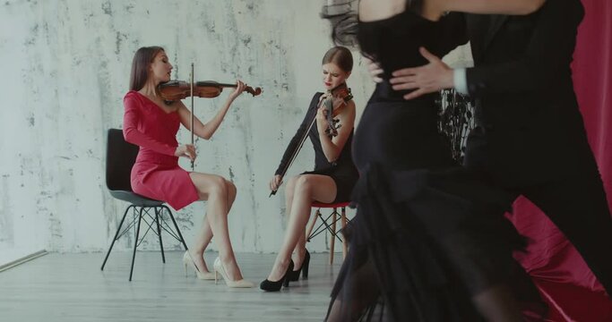Two elegant girls playing the violin, couple of dancers performs tango indoor