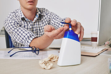 Businessman applying sanitizer refreshing gel on his hands before working on computer at office desk