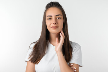 Picture of stylish Attractive European young woman with long chestnut hair keeps hand on neck. European young woman isolated over white background.