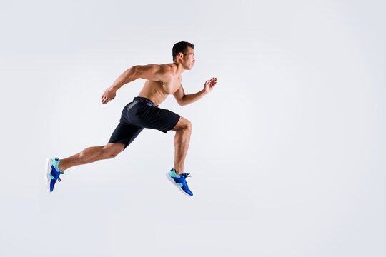 Full body profile photo of handsome sportsman dark skin guy naked chest jump high up running fast sprint workout exercise fat burn wear shorts sneakers isolated white color background