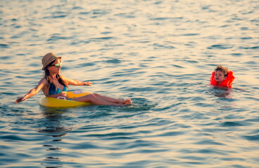 Two happy brother and sister rest on the sea. Smiling girl swimming in a circle in the sea. Little boy in an inflatable vest swims with his family