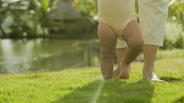baby first step on a grass outdoor supported by mother