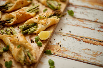 Baked green asparagus wrapped in puff pastry. Served on wooden board. With copy space
