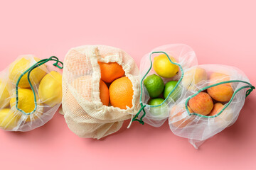 Fruits and citrics in reusable eco-friendly mesh bags on pink background. Zero waste shopping.