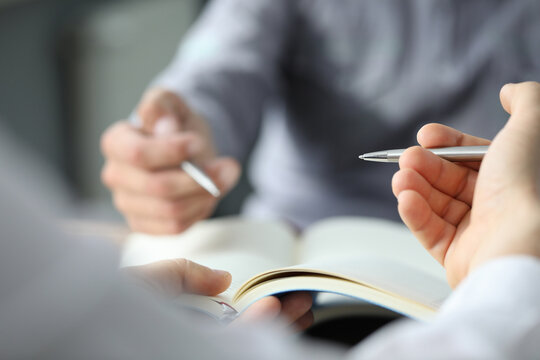 Close up of male hands holding sheet of paper with pen while sitting at the desk in the office. Work and business concept