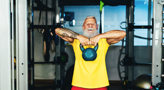 Hipster senior man training inside gym - Mature tattooed person having fun doing workout exercises in sport fitness club - Active joyful elderly lifestyle and fit concept - Focus on face