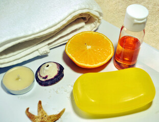 Orange spa composition of orange soap, citrus shampoo, salt, seashells, candles, organic cotton towels against ecru background. Tonic and vitaminizing products. Organic cosmetics