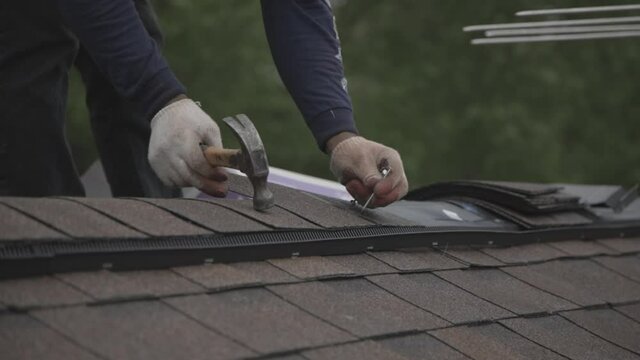 Roofer hammering in a shingle on roof