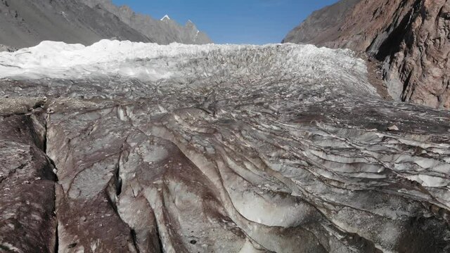 Down-looking view of the stunning Passu glacier surrounded by arid mountains, with rocks, snowy peaks in the background, blocks of ice and a beautiful blue sky, Giglit Baltistan region, Pakistan