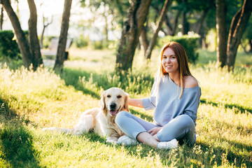 a young woman and a golden retriever dog sit on the grass in the park