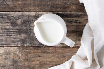 Milk jug on a wooden background, top view, rustic style.