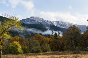View on snowy mountains clouds and autumn colors forest. Changing season landscape