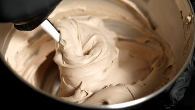 The cook is mixing beige creme in in steel bowl for making dessert, close-up. Sweet food preparation. Making mousse dessert.
