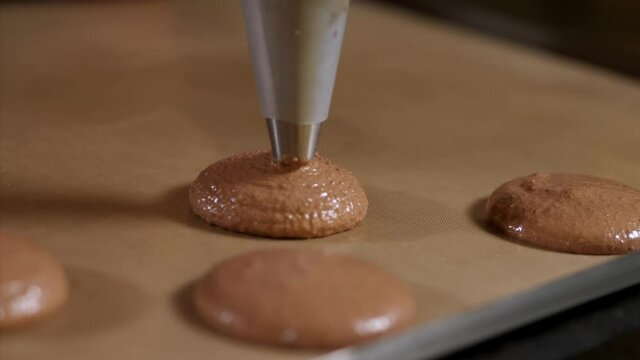 Chef making base for preparation macaron dessert. Close-up of extruding brawn creme from piping bag on metal tray for baking base of macaron dessert.
