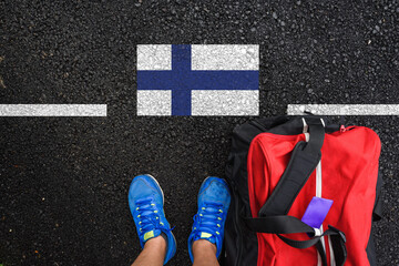 a man with a shoes and travel bag is standing on asphalt next to flag of Finland and border