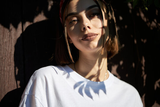 Fashion portrait of a sexy brunette woman with a make up wearing white clothes outside with tree shadows on a face