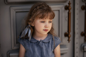 
girl in a gray dress stands at the gray wooden door in summer