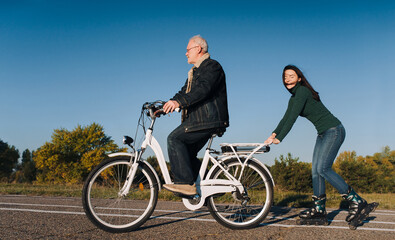 Young smiling caucasian girl on roller skates and a man on a white electric bike fun ride together. Concept of active leisure and hobbies. Father and daughter.