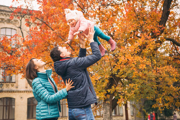 Casual family couple with daughter on a free time in park. Autumn cloudy weather with fallen leafs....