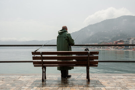 Fisherman with waterproof jacket on the pier of the Alassio seafront, in the sun after a summer rain