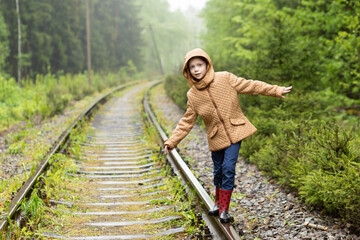Cute red hair girl walking on railway alone, she is sad. The only one way to travel in coronavirus quarantine time. Rainy weather.