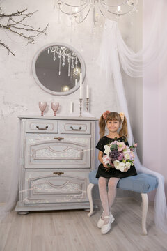 Pretty little girl holding a bunch of colouful flowers in her hands against a backdrop of closed curtains with copyspace