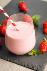 Glass of fresh strawberry milkshake, smoothie and fresh strawberries on pink, white and wooden background. Healthy food and drink concept.