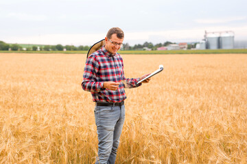 Farmer writing on a document the wheat development plan. Farmer checking wheat field progress. 