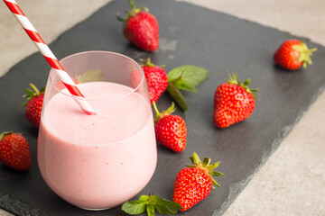 Glass of fresh strawberry milkshake, smoothie and fresh strawberries on pink, white and wooden background. Healthy food and drink concept.