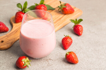 Glass of fresh strawberry milkshake, smoothie and fresh strawberries on pink, white and wooden background. Healthy food and drink concept.